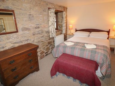 A bedroom with a double bed bedside tables lamps a chest of drawers and stone wall at The Old Stable in Pontfaen near Fishguard