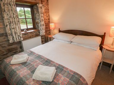 A bedroom with a double bed white bedding folded towels bedside tables lamps and a window at The Old Stable in Pontfaen near Fishguard