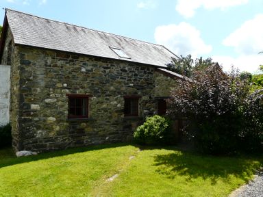 A stone building with two windows and a roof window surrounded by grass and bushes at The Old Stable in Pontfaen near Fishguard