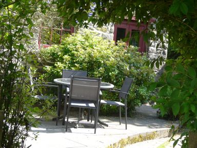 An outdoor patio with a round glass table and four chairs surrounded by bushes and trees at The Old Stable in Pontfaen near Fishguard
