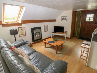 A living room with a grey leather sofa wooden coffee table television and wooden door at The Loft in Pontfaen near Fishguard