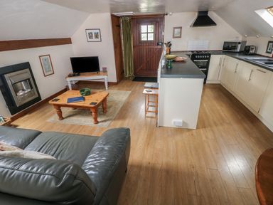 A living room with a wooden coffee table a TV a stove and a kitchen area at The Loft in Pontfaen near Fishguard