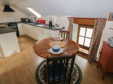 A kitchen with a round wooden dining table set for two beside a window with floral curtains at The Loft in Pontfaen near Fishguard