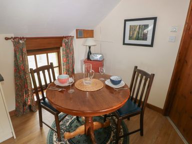A dining area with a round wooden table set for two with bowls and glasses near a window with curtains at The Loft in Pontfaen near Fishguard