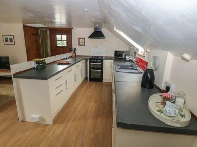 A kitchen with black countertops white cabinets a stove a sink a kettle and kitchen utensils at The Loft in Pontfaen near Fishguard