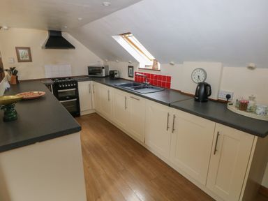 A kitchen with white cabinets black countertops a stove microwave toaster and a window at The Loft in Pontfaen near Fishguard