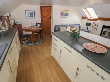 A kitchen with cabinets and a countertop next to a dining area with a round table and chairs at The Loft in Pontfaen near Fishguard