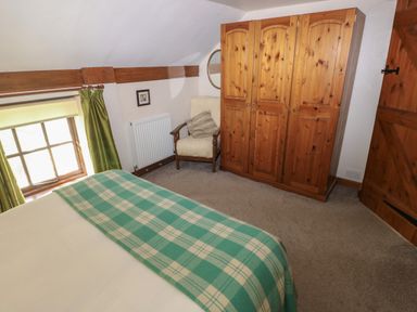 A bedroom with a wooden wardrobe an armchair green curtains and a bed with a green checked blanket at The Loft Pontfaen near Fishguard