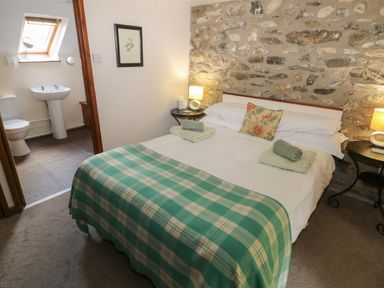 A bedroom with a double bed covered with a checkered green blanket and two rolled towels with a floral pillow by a stone wall at The Loft in Pontfaen near Fishguard