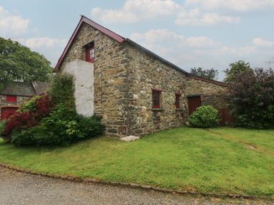 A stone building with red-framed windows and doors surrounded by green grass and bushes at The Loft in Pontfaen near Fishguard