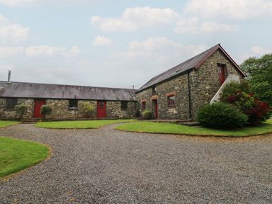A gravel driveway leading to two stone buildings with red doors and windows at The Loft in Pontfaen near Fishguard