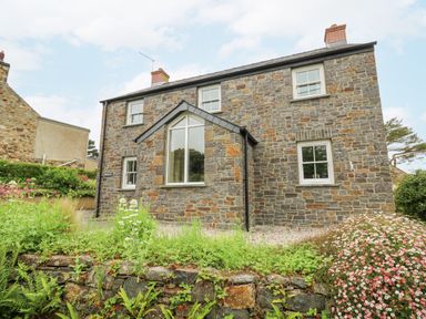 A stone house with white framed windows and a garden with flowers at Beachway in Brynhenllan near Dinas Cross
