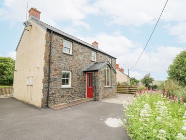 Stone house with red door driveway and flowering plants at Beachway Brynhenllan near Dinas Cross