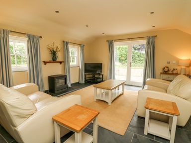 A living room with two cream sofas wooden coffee and side tables a television and blue curtains at Beachway Brynhenllan near Dinas Cross