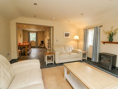 A living room with two white sofas a wooden coffee table a floor lamp a fireplace and a dining area in the background at Beachway in Brynhenllan near Dinas Cross