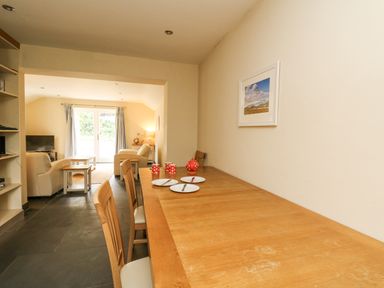 A dining area with a wooden table set with plates cups and a teapot adjacent to a living room with armchairs a coffee table and a television at Beachway in Brynhenllan near Dinas Cross