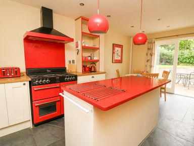 A kitchen with a red stove and red countertop island near a dining table and glass sliding door at Beachway in Brynhenllan near Dinas Cross