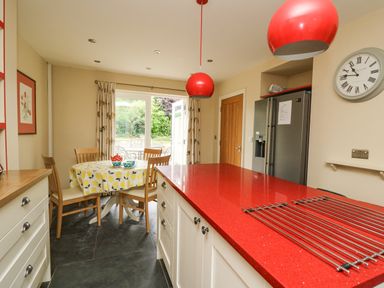 A kitchen with a red countertop island wooden dining chairs round table with a yellow tablecloth and a glass door leading outside at Beachway Brynhenllan near Dinas Cross