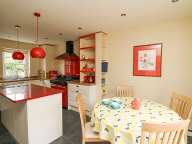A kitchen with red pendant lights and appliances and a dining table with yellow patterned tablecloth at Beachway in Brynhenllan near Dinas Cross