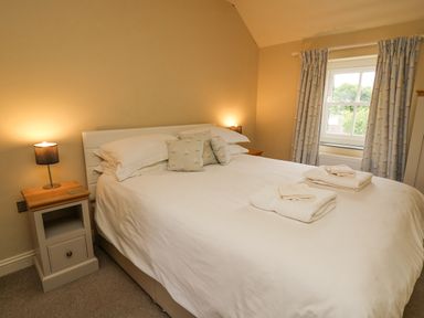 A bedroom with a double bed with white bedding and towels on it with nightstands and lamps on each side and a window with curtains at Beachway Brynhenllan near Dinas Cross