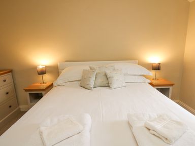 A bedroom with a double bed white linens bedside tables lamps and folded towels at Beachway Brynhenllan near Dinas Cross