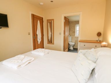 A bedroom with a bed towels a dresser and an open door leading to a bathroom at Beachway Brynhenllan near Dinas Cross