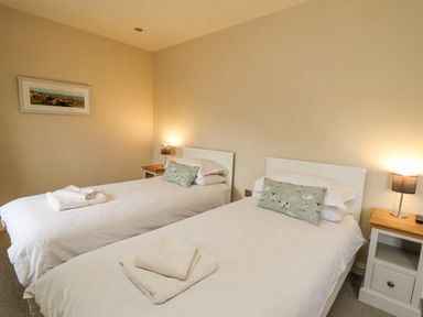 A bedroom with two single beds with white bedding and patterned pillows two bedside tables with lamps and folded towels on the beds and a framed picture on the wall at Beachway in Brynhenllan near Dinas Cross