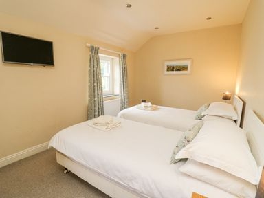 A bedroom with two single beds a wall mounted TV and a window with curtains at Beachway in Brynhenllan near Dinas Cross