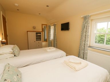 A bedroom with two single beds a wardrobe a wall mirror a window with curtains and a mounted television at Beachway in Brynhenllan near Dinas Cross