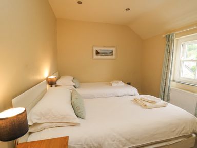 A bedroom with two single beds bedside lamps a window with curtains and folded towels on Beachway in Brynhenllan near Dinas Cross