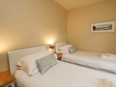 A bedroom with two single beds with white bedding and green cushions with seashell designs and a framed beach picture on the wall at Beachway in Brynhenllan near Dinas Cross