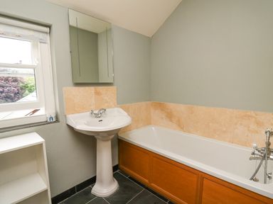 A bathroom with a pedestal sink, bathtub with wooden panel, mirror, and window at Beachway Brynhenllan near Dinas Cross
