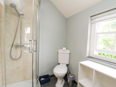 A bathroom with a shower enclosure a toilet a window and a white storage unit at Beachway in Brynhenllan near Dinas Cross