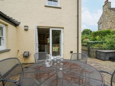An outdoor patio area with a metal table and chairs and a glass jug and glasses near doors leading inside at Beachway Brynhenllan near Dinas Cross