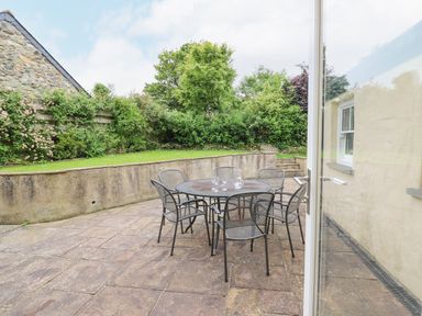 An outdoor patio with a round metal table and six chairs surrounded by a low wall and greenery at Beachway Brynhenllan near Dinas Cross