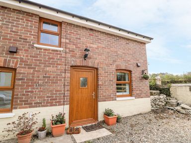The front entrance of a brick house with a wooden door and three windows with flower pots outside at Field View in Llanybydder