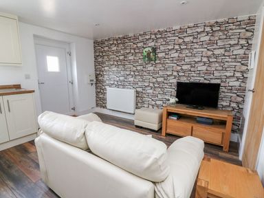 A living room with a white sofa a wooden TV stand with a television a small ottoman and a stone effect feature wall at Field View in Llanybydder