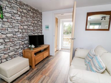 A living room with a white sofa with pillows a wooden media unit with a television and a stone patterned wall at Field View in Llanybydder