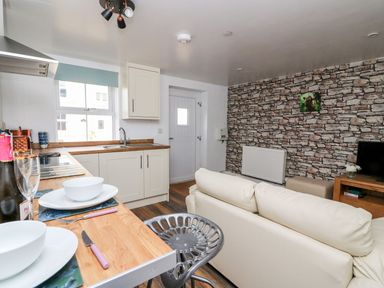 A kitchen area with cream cabinets and wooden countertops next to a living room with a cream sofa and a stone patterned wall at Field View in Llanybydder