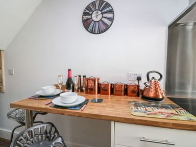 A kitchen countertop with copper canisters labeled biscuits coffee sugar and tea a copper kettle two place settings a bottle of prosecco and a wall clock at Field View in Llanybydder