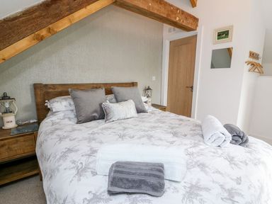 A bedroom with a double bed with pillows and folded towels under a wooden ceiling beam at Field View in Llanybydder
