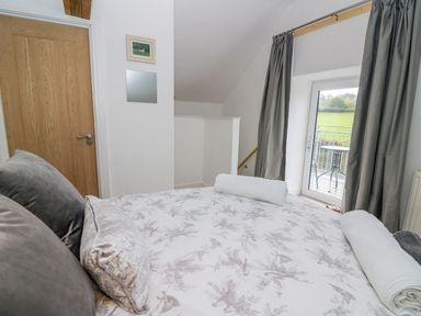 A bedroom with a bed two pillows two rolled towels a wooden door a window with curtains and a balcony at Field View in Llanybydder