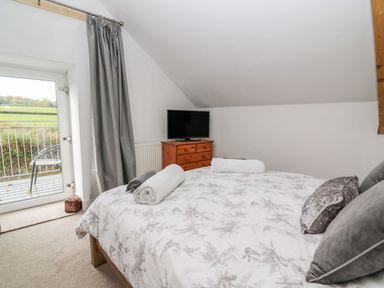 A bedroom with a bed folded towels a wooden dresser with a television and a door with grey curtains at Field View in Llanybydder