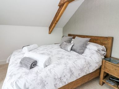 A bedroom with a wooden bed frame gray pillows white and gray towels on the bed and a wooden bedside table at Field View in Llanybydder