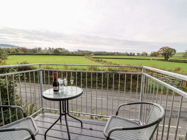 A balcony with two chairs and a table with a bottle and glasses overlooking green fields at Field View in Llanybydder