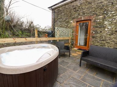 An outdoor patio with a hot tub two chairs and a glass door in a stone building at Field View in Llanybydder