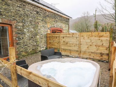 An outdoor area with a bubbling hot tub black wicker chairs and a stone wall at Field View in Llanybydder