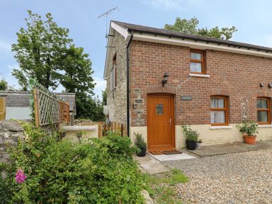 A brick and stone house with wooden door and windows surrounded by plants and gravel at Garden View in Llanybydder