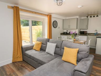 A living room with gray sofa and yellow pillows next to a dining table and kitchen at Garden View in Llanybydder