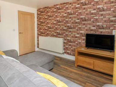 A room with a gray sofa a wooden door a radiator and a TV on a wooden stand at Garden View in Llanybydder